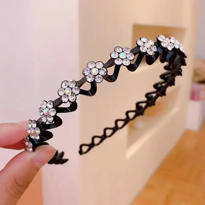 A black rhinestone wave headband is being held by a hand against a light background.