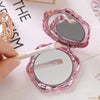 A pink vintage rose design double-sided pocket makeup mirror is shown being held and used.