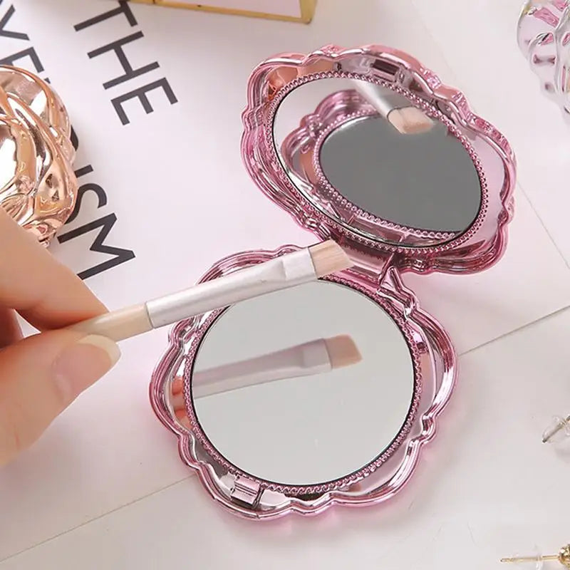 A pink vintage rose design double-sided pocket makeup mirror is shown being held and used.