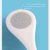 A white reusable tongue cleaner brush with a textured head is shown against a light blue background.