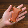 A natural wood facial and scalp massage comb with gold-colored ball attachments is held in a hand.