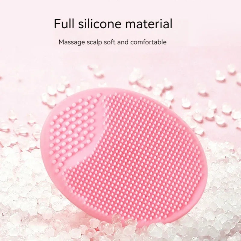 A pink silicone facial cleansing brush with textured surfaces resting on white exfoliating beads.
