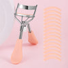 A professional stainless steel eyelash curler set with pink silicone applicators shown against a light pink background.