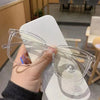 Una mano sostiene unas gafas cuadradas vintage y transparentes anti-luz azul sobre una superficie blanca.