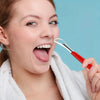 Una mujer usa un raspador de lengua de acero inoxidable rojo para la higiene bucal.