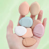 A hand holds several mini finger puff foundation applicator tools in various shades of beige and pink.
