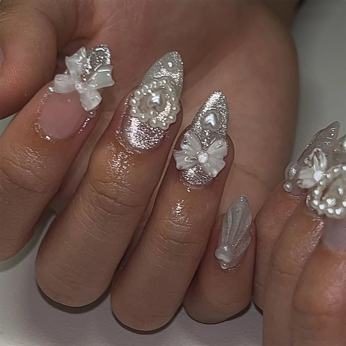 A hand displays 24 pink heart pearl press-on fake nails with glitter accents on fingers.