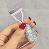 A hand holds a pink professional eyelash curler set with a sparkly silver eyelash curler attached.