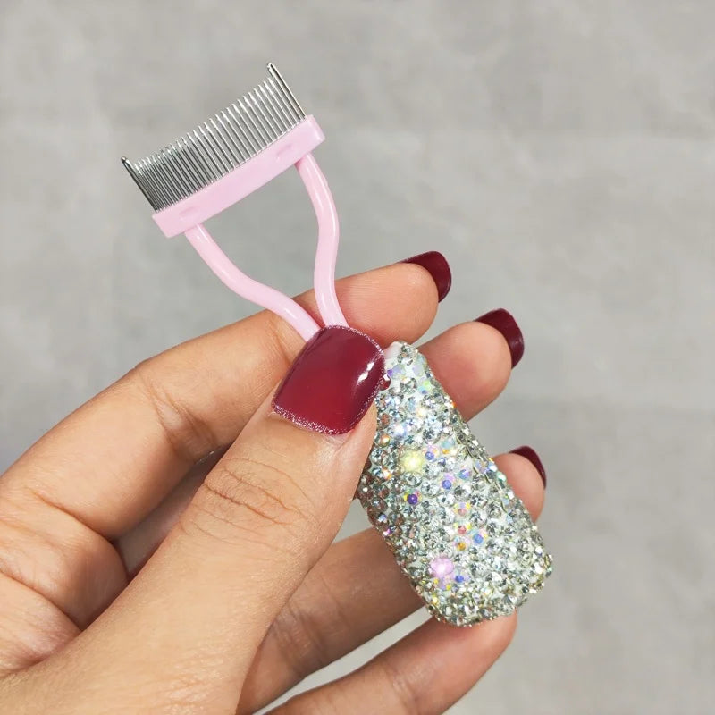 A hand holds a pink professional eyelash curler set with a sparkly silver eyelash curler attached.