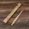 A bamboo toothbrush packaged in natural paper, shown next to a wooden brush.