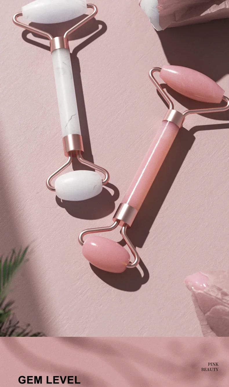 A set of pink and white resin facial massage rollers with rose gold handles resting on a light pink surface.