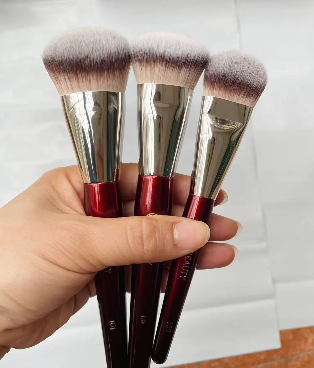 Trois pinceaux de maquillage à fondation liquides anglés avec ferrules argentées et poils roses tenus dans une main.