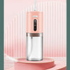 A pink portable electric water flosser with a silver body is displayed on a light pink stand against a striped background.