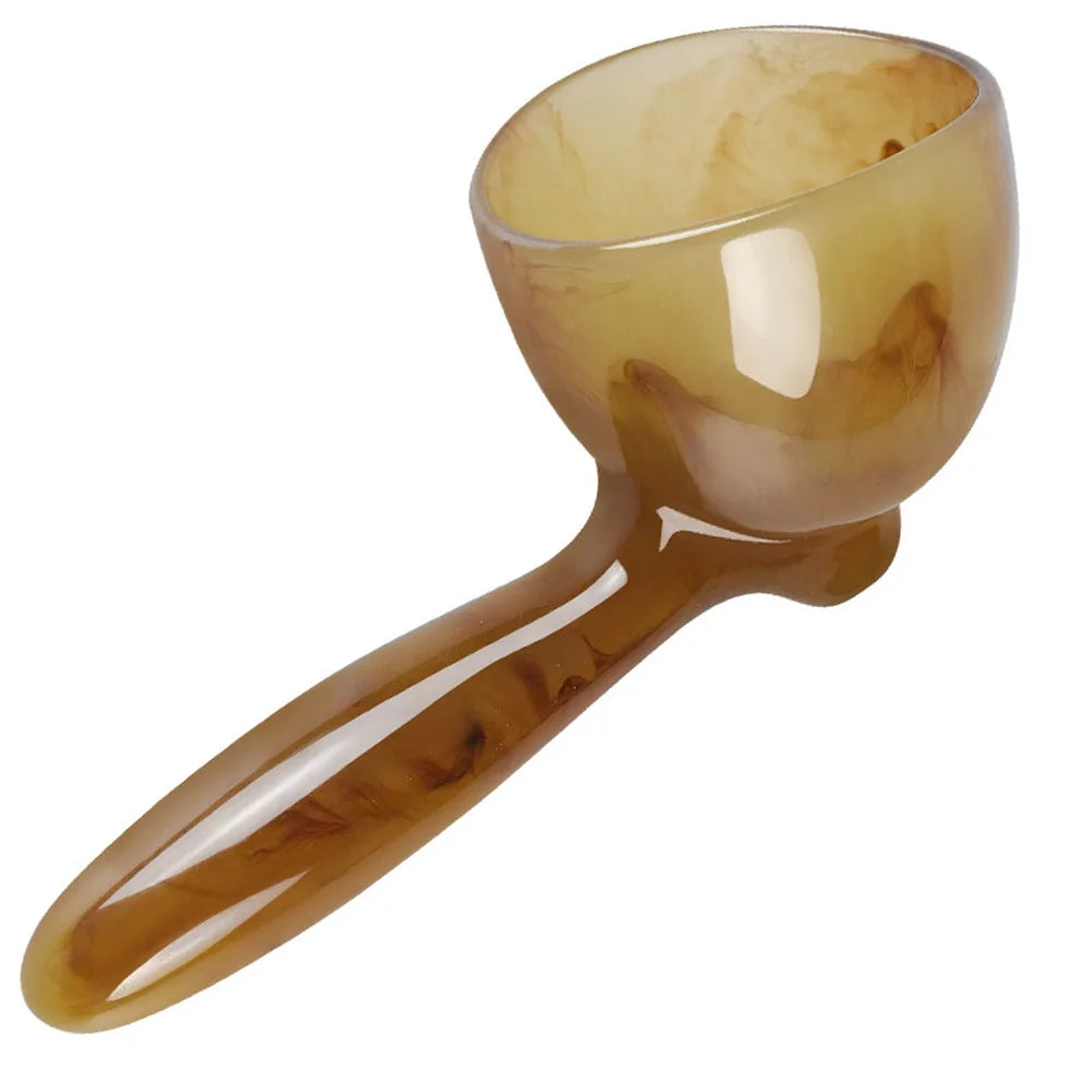 A translucent amber resin gua sha scraping massage tool with a rounded bowl and elongated handle.