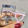 A hand holds a professional eyelash curler set with silver metal and pink plastic components.