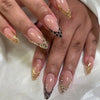 A close-up of a hand displaying pink flower almond press on nails with gold accents and black leopard print details.