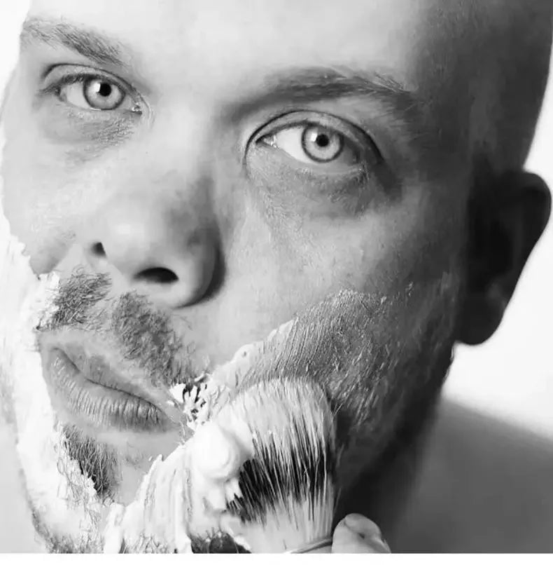 Primer plano en blanco y negro de un hombre afeitándose la barba con un set de cepillo de madera
