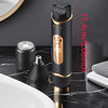A black electric body hair trimmer with a gold accent is shown next to its detachable head and on a marble surface.