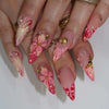 Gros plan d'une main montrant un ensemble d'ongles press-on roses à l'amande française avec des accents floraux.