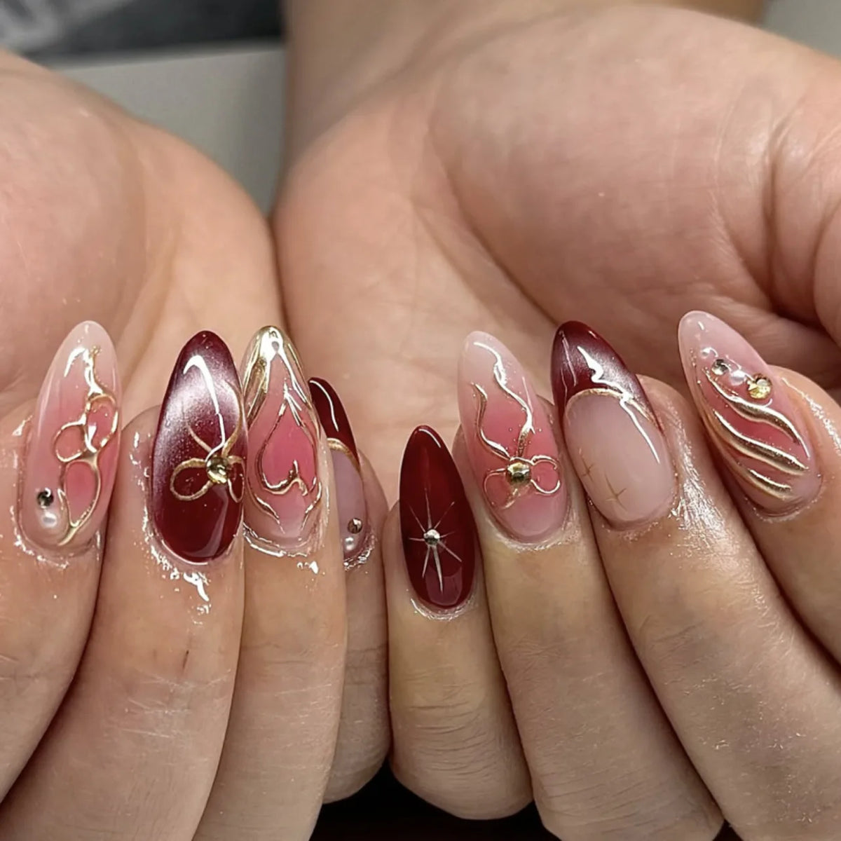A close-up of hands displaying 24 press-on nails with pink and gold floral designs on a natural nail bed.