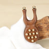 A natural wood facial and scalp massage comb with gold-colored spherical tips is held by a hand.