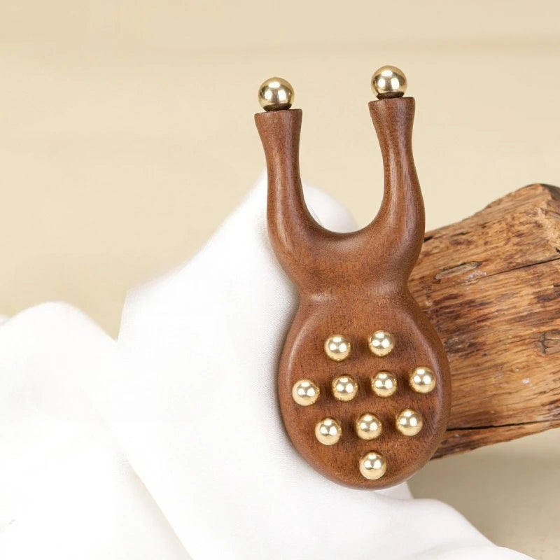 A natural wood facial and scalp massage comb with gold-colored spherical tips is held by a hand.