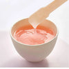 Un bâton en bois est utilisé pour appliquer un produit liquide rose d'un bol pour une épilation naturelle.