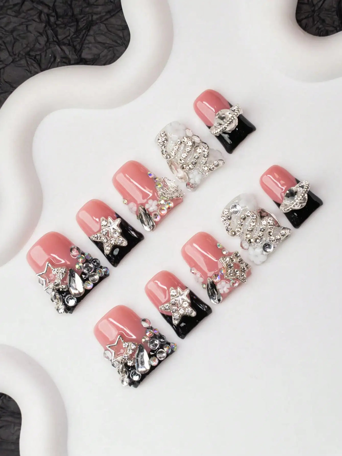 Un set de uñas postizas Y2K con diseños rosa y negro, adornados con cristales y estrellas.