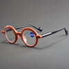 Un par de gafas de lectura con marco naranja y brazos negros sobre una superficie gris.