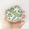 A hand holds an air cushion makeup puff set with a storage box featuring a green and white patterned puff.