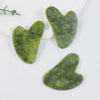 Three jade gua sha tools in various shades of green resting on a white surface.