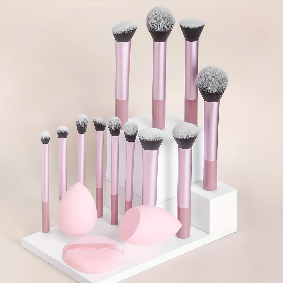 Un juego de doce pinceles de maquillaje profesionales en rosa y gris exhibidos sobre una superficie blanca.
