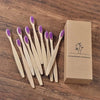 Une boîte contenant dix brosses à dents en bambou naturelles posées sur une surface en bois.