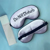 A lavender silk sleep mask embroidered with Do Not Disturb text is shown next to its packaging.
