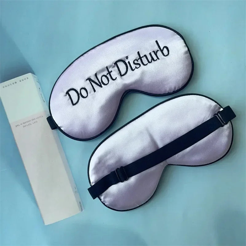 A lavender silk sleep mask embroidered with Do Not Disturb text is shown next to its packaging.