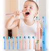 A baby is using a pink electric toothbrush while several blue and pink toothbrushes are displayed.