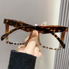 A hand holds a pair of tortoiseshell reading glasses with clear frames and blue light protection.