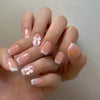 A hand displays a set of white French style press-on nails with a coffin shape and delicate floral accents.