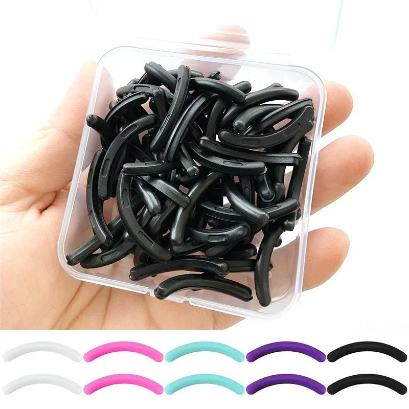 A hand holds a clear plastic container filled with black reusable silicone eyelash curler pads.