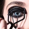 Close-up of an eye being curled with a black metal eyelash curler.