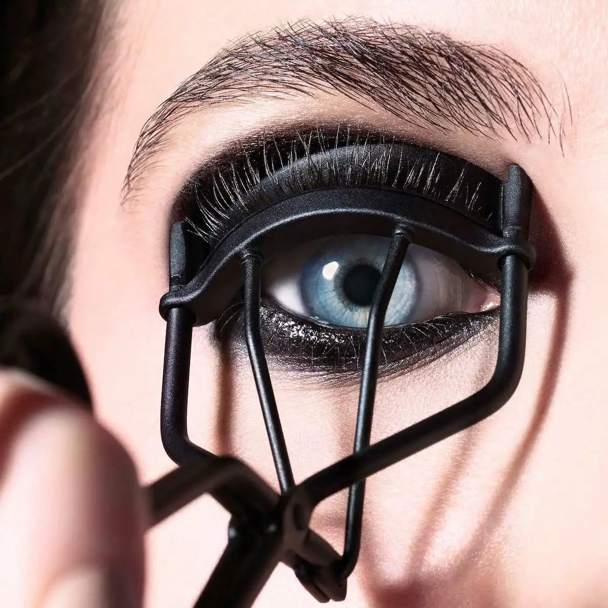 Close-up of an eye being curled with a black metal eyelash curler.