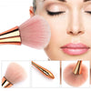 A rose gold dusting and makeup removal brush set shown next to a woman's face.