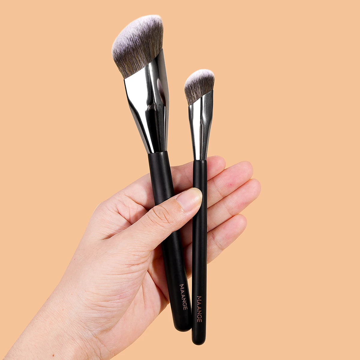 A hand holds a set of black makeup brushes with grey bristles against a beige background.