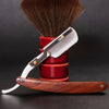 A professional shaving razor with a silver handle and wood grip rests on a red cylindrical stand, next to a shaving brush.