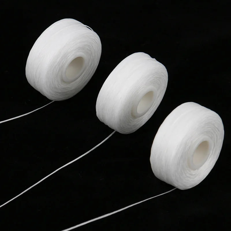 Three white dental floss spools lying on a black surface, with thin strands of floss extending from them.