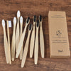 A box containing a set of ten natural bamboo toothbrushes and a cleaning instruction card on a wooden surface.