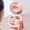 A hand holds a circular LED makeup mirror showing a woman's face with luminous skin and pink lips.