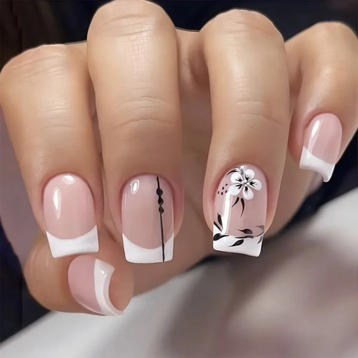 A close-up of a hand displaying press-on acrylic flower nails with white and black floral designs.
