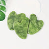 Three heart-shaped jade gua sha tools in a light green color resting on a white surface.