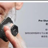 A hand is using a black silicone facial cleaning brush for pre-shave exfoliation on a man's face.